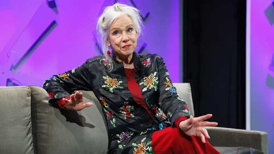 Marianne Schwirren als Frau Frélange, auf einer Couch sitzend.